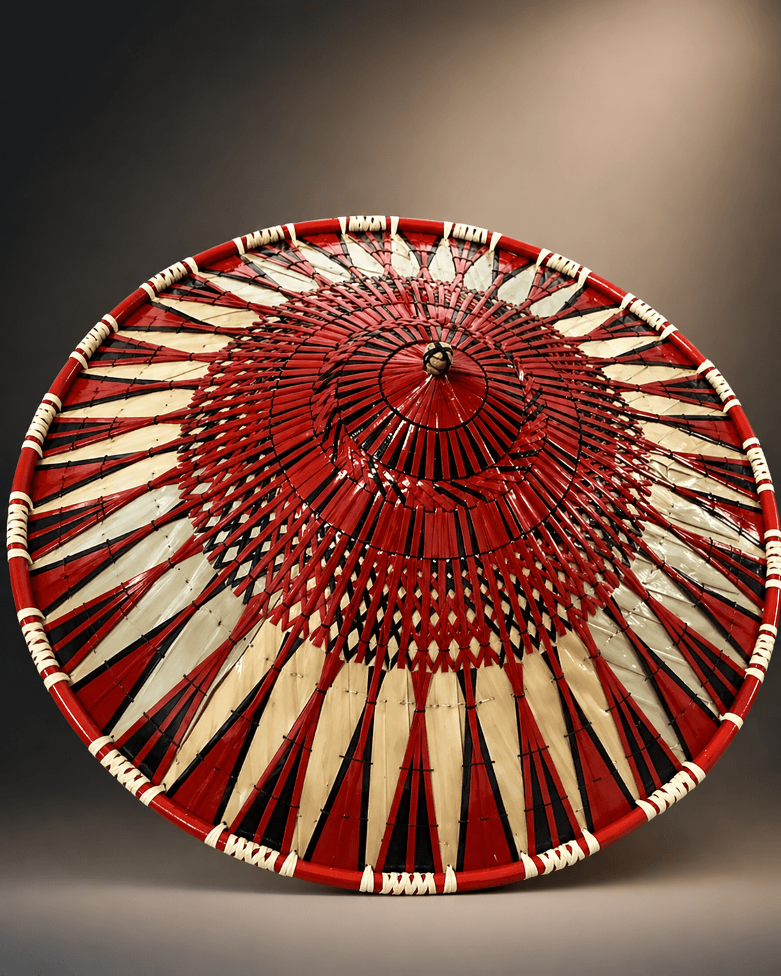 Intricately woven red, black, and cream conical hat featuring a bold, radiating geometric design.